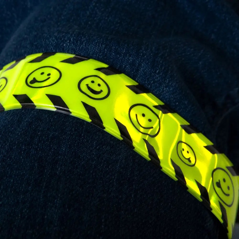 Close-up of high visibility reflective snap wristband glowing under light at night, fluorescent yellow surface with smiley pattern for enhanced safety