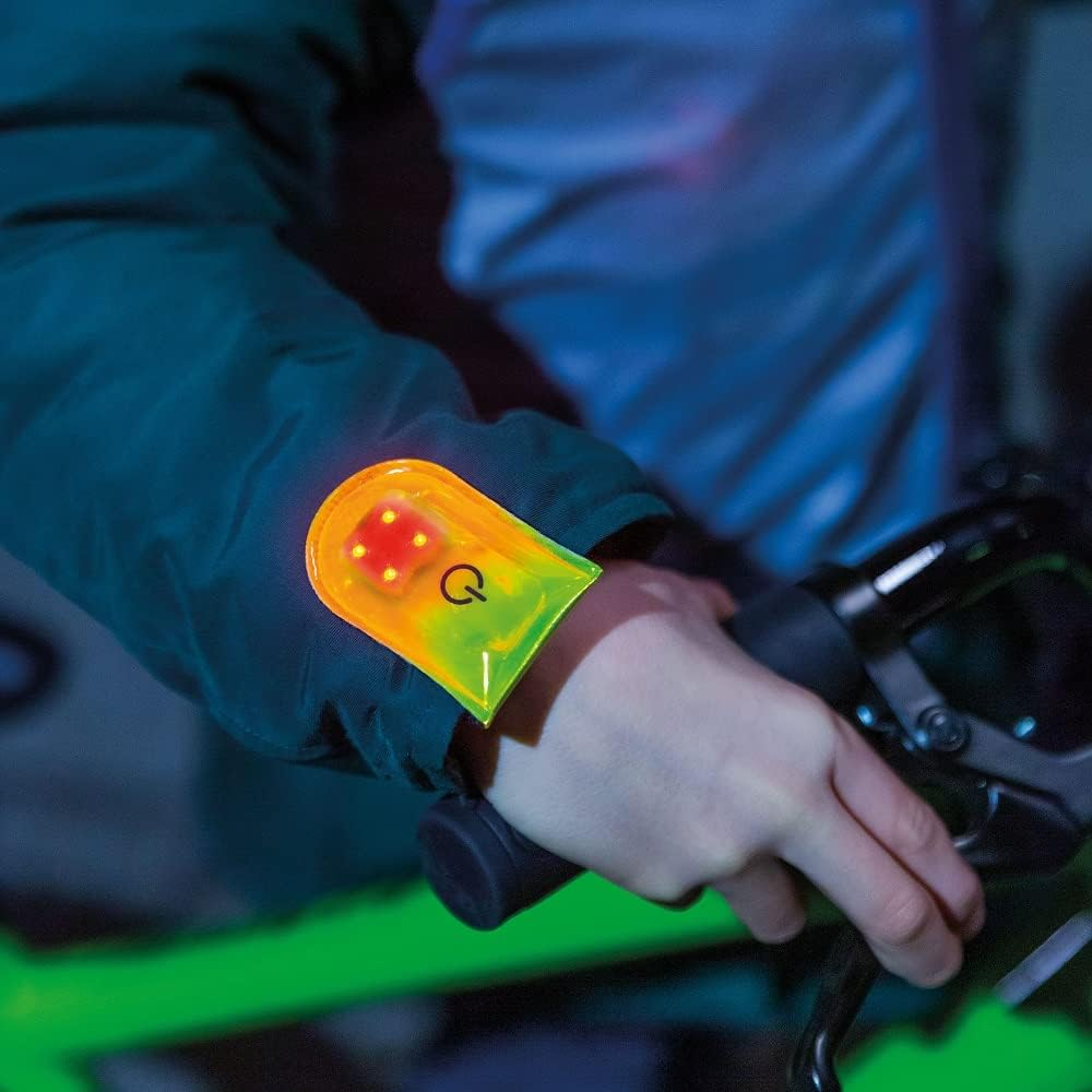 Cyclist wearing a magnetic clip LED safety light on jacket sleeve while riding at night for increased visibility