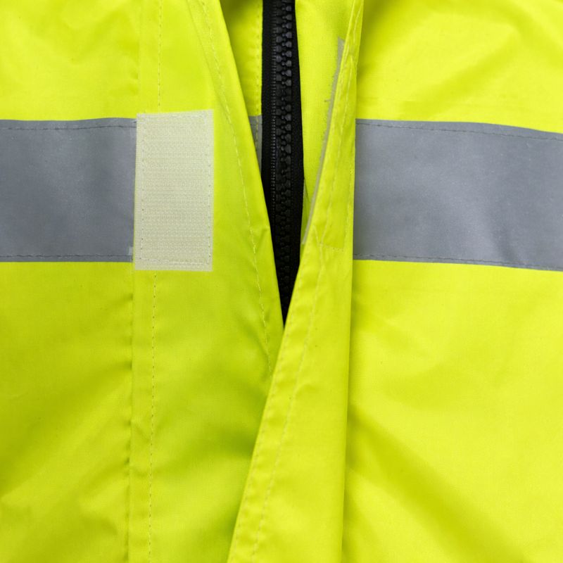 Close-up of hi-vis rain jacket double storm flap with waterproof zipper and reflective tape on fluorescent yellow fabric