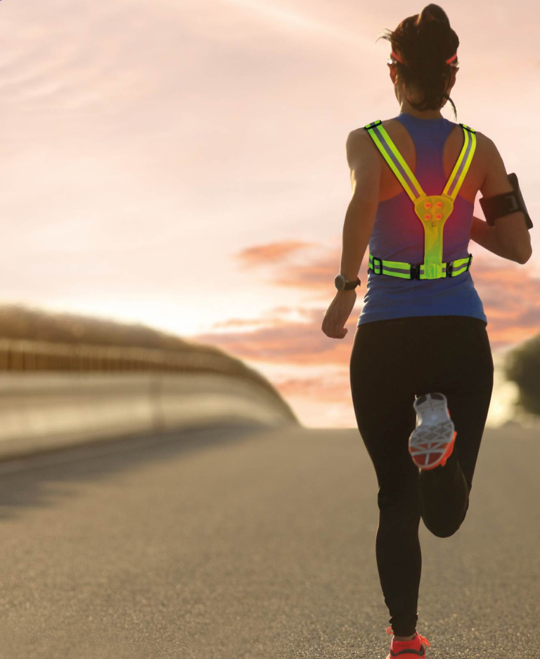 Runner wearing LED reflective running harness during evening outdoor workout, showing back LED lights for increased night visibility